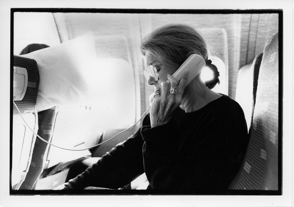 This black and white photo displays Gloria Steinem talking on the phone on an airplane.