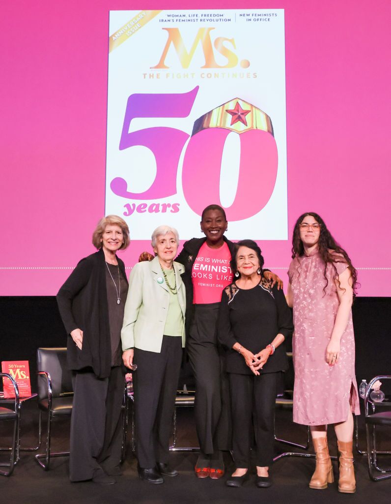 Standing in front of a pink screen with a magazine cover celebrating 50 years of Ms. are Kathy Spillar, Eleanor Smeal, Michele Bratcher Goodwin, Dolores Huerta and Carmen Rios.