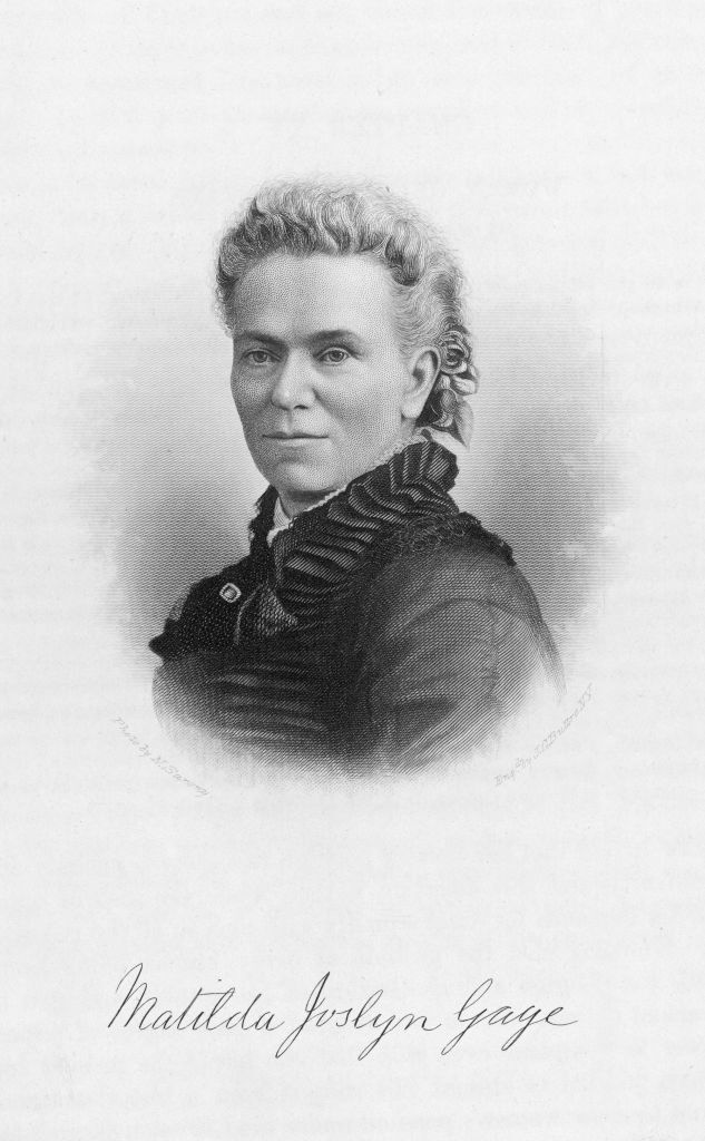 In this antique black-and-white photo of Matilda Joslyn Gage, she wears her hair up and a black collared dress. Below her headshot her name is written in cursive. 